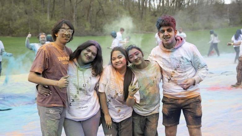 Five students covered in colorful dust smile for the camera.